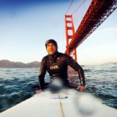 USA, California, San Francisco, Fort Point, surfer sitting on his surfboard under the Golden Gate Bridge at Sunset